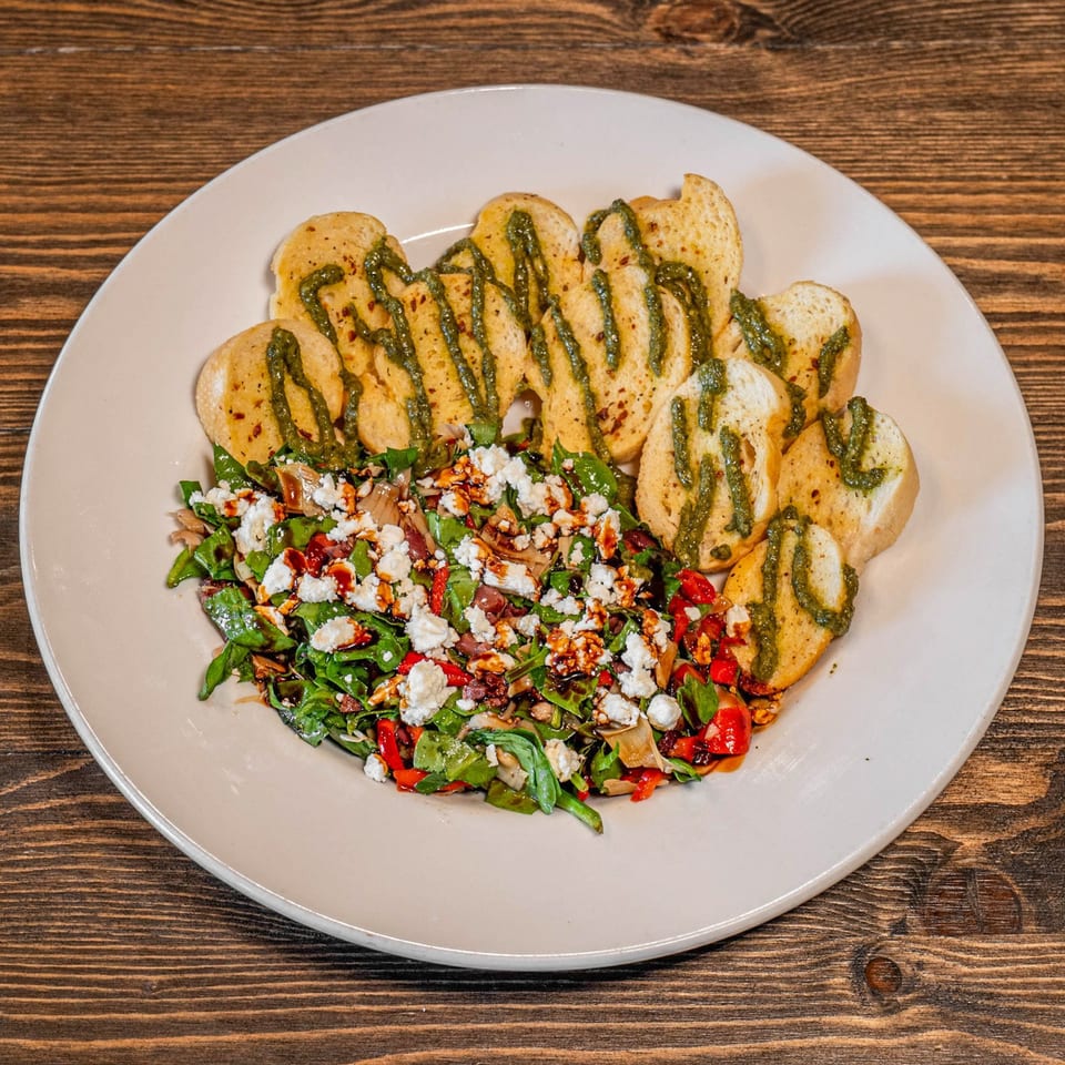 Plate of toasted bread drizzled with green sauce alongside a colorful salad topped with crumbled cheese and balsamic glaze.
